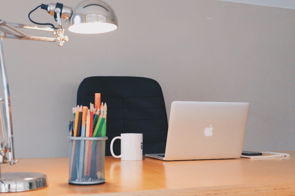 Laptop workstation set up on a desk with a desk lamp and notebooks