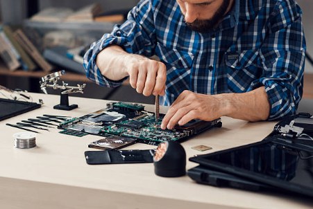 Technician repairing a laptop motherboard with a screwdriver