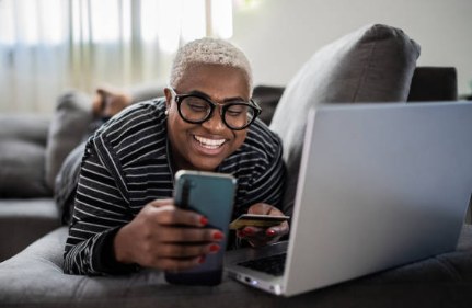 Happy customer smiling while using her laptop and phone at home